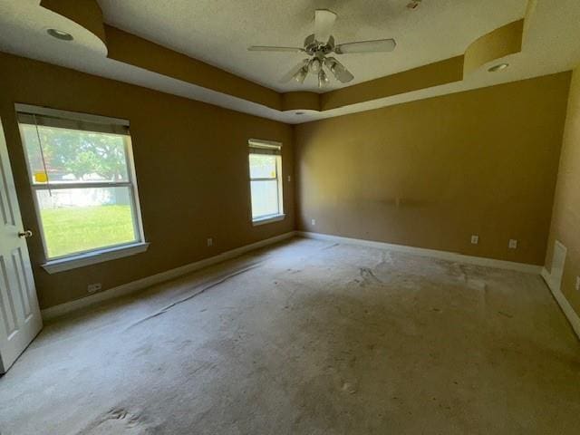 carpeted spare room featuring baseboards, a ceiling fan, a tray ceiling, and a textured ceiling