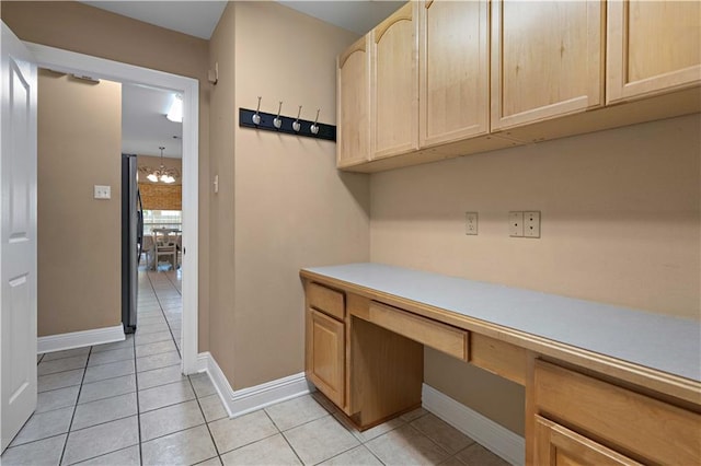 unfurnished office featuring built in desk, light tile patterned flooring, a notable chandelier, and baseboards