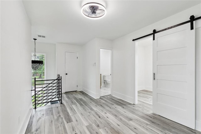 7230 Bullard Ave, New Orleans, LA 70128 - unfurnished room featuring a barn door, light wood-style flooring, and baseboards
