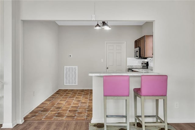 kitchen with a breakfast bar, appliances with stainless steel finishes, light countertops, visible vents, and a peninsula