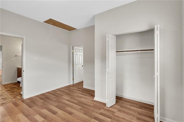 unfurnished bedroom with attic access, wood finished floors, baseboards, and a closet