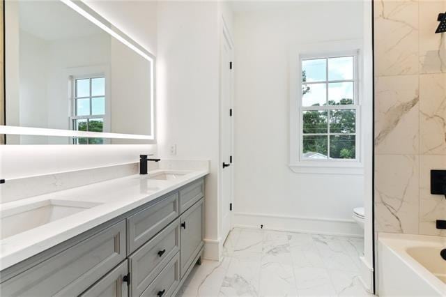 full bath featuring double vanity, marble finish floor, toilet, a bath, and a sink