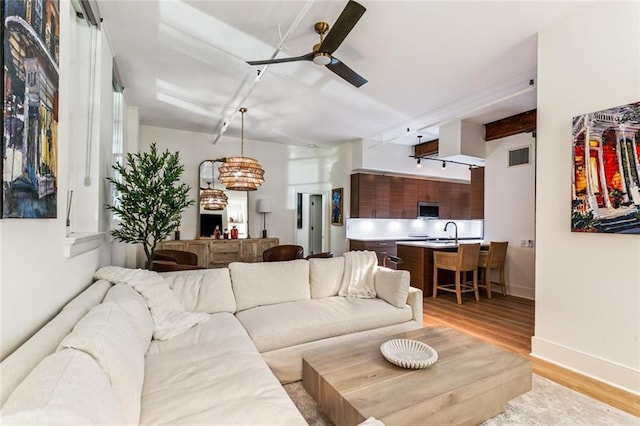 living area featuring baseboards, visible vents, ceiling fan, and light wood finished floors