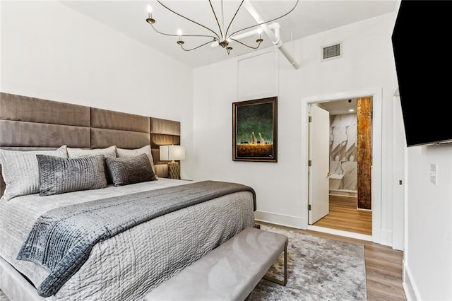bedroom featuring visible vents, baseboards, an inviting chandelier, wood finished floors, and ensuite bath