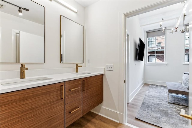 bathroom featuring wood finished floors, baseboards, a chandelier, and a sink