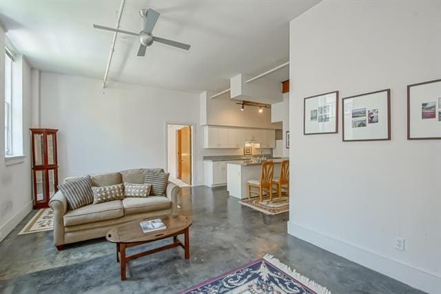 living room featuring baseboards, a ceiling fan, concrete flooring, and a wealth of natural light