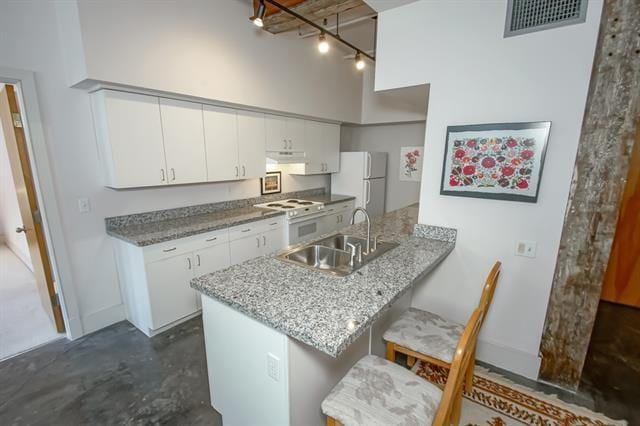 kitchen with white appliances, concrete floors, a sink, visible vents, and a peninsula