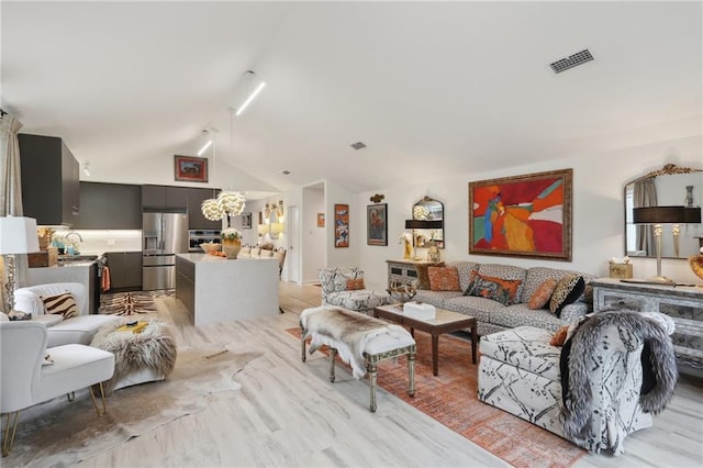 living area with light wood finished floors, visible vents, and vaulted ceiling