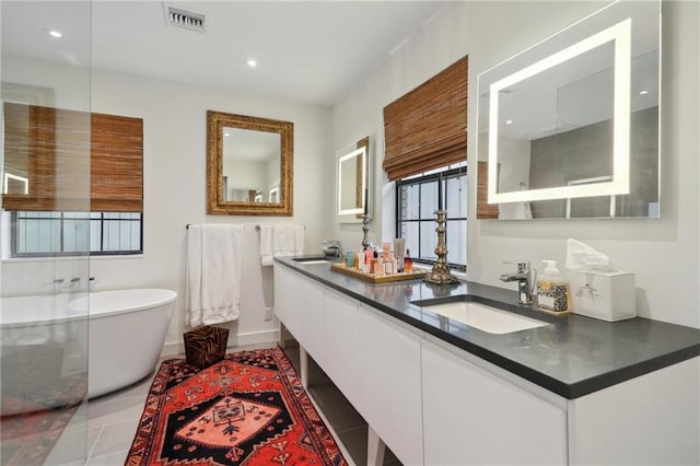 bathroom featuring double vanity, visible vents, a soaking tub, and a sink