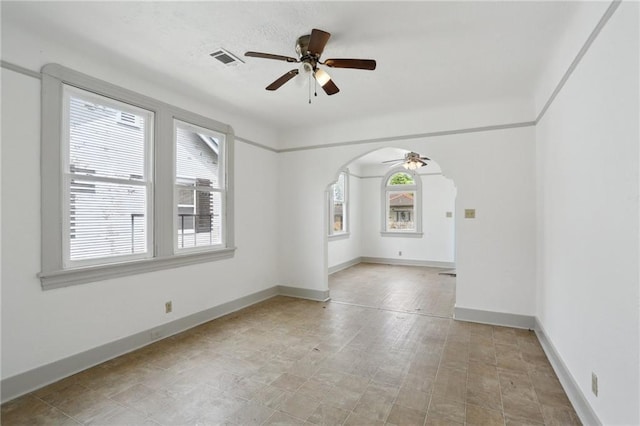 spare room with visible vents, a ceiling fan, baseboards, and arched walkways