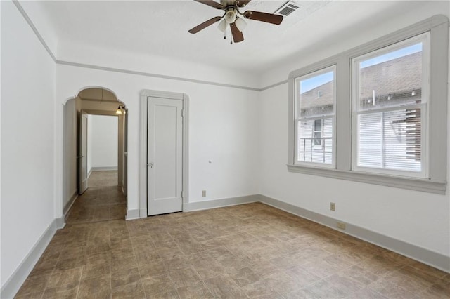 unfurnished room with visible vents, ceiling fan, baseboards, and arched walkways