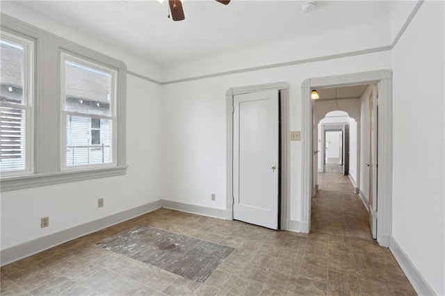 unfurnished room with baseboards, arched walkways, ceiling fan, and plenty of natural light