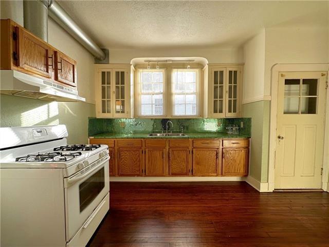 kitchen with a sink, dark wood-style flooring, under cabinet range hood, white range with gas cooktop, and backsplash