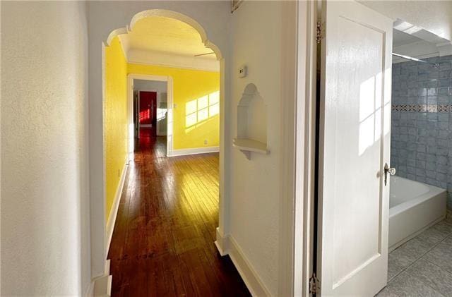 corridor with hardwood / wood-style flooring, baseboards, and arched walkways