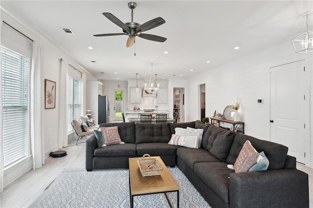 living area featuring visible vents, light wood-type flooring, recessed lighting, ornamental molding, and ceiling fan with notable chandelier