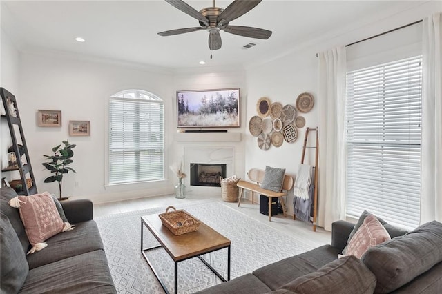 living room featuring a premium fireplace, crown molding, visible vents, and a ceiling fan