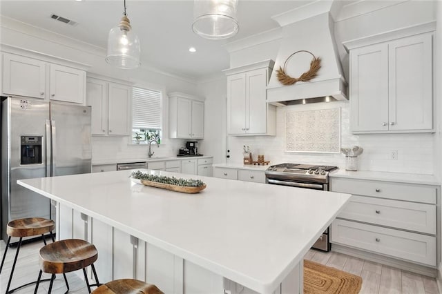 kitchen with crown molding, visible vents, stainless steel appliances, a kitchen island, and premium range hood