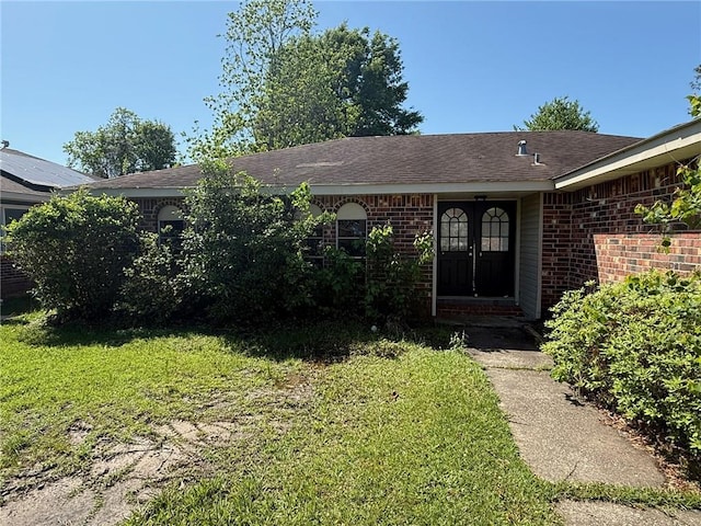 entrance to property with brick siding, roof with shingles, and a lawn