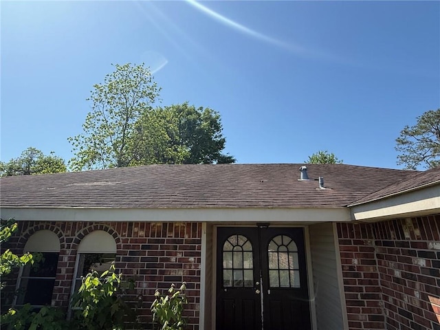 doorway to property featuring roof with shingles and brick siding