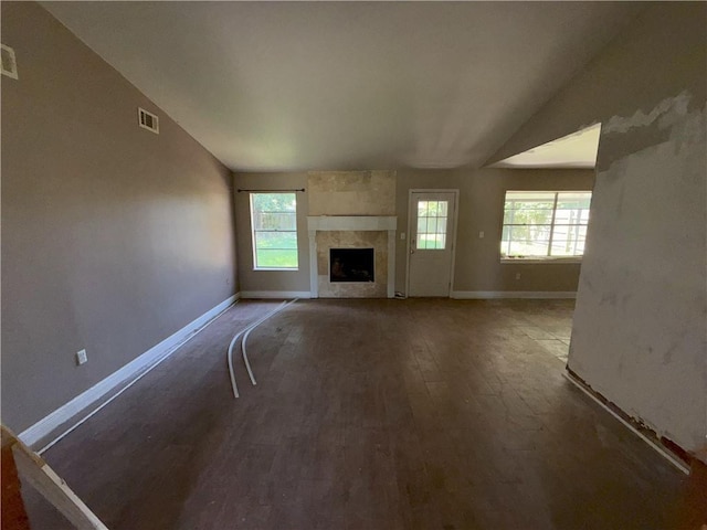 unfurnished living room with a fireplace, lofted ceiling, visible vents, baseboards, and wood finished floors