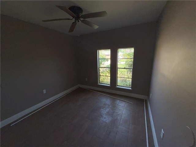 spare room featuring baseboards, ceiling fan, and dark wood-style flooring