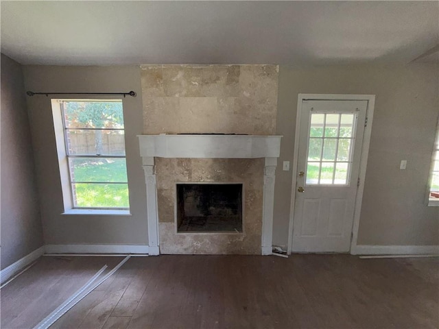 unfurnished living room featuring a tile fireplace, wood finished floors, and baseboards