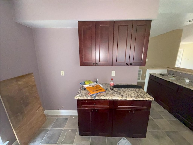 kitchen featuring reddish brown cabinets, light stone countertops, tile patterned flooring, and baseboards