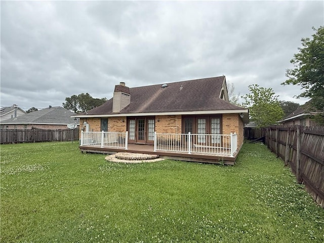 back of property with a deck, brick siding, a chimney, and a lawn