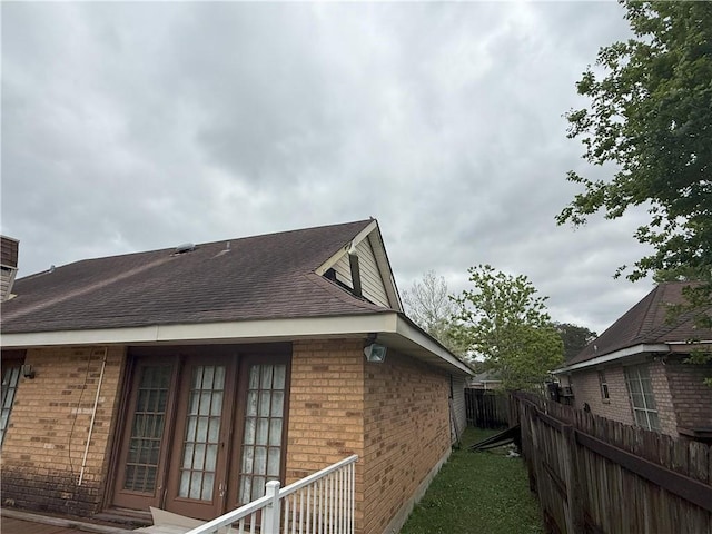 view of home's exterior with a chimney, brick siding, fence, and roof with shingles