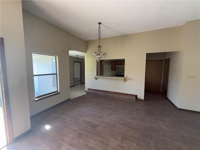 unfurnished living room featuring a notable chandelier, wood finished floors, and baseboards