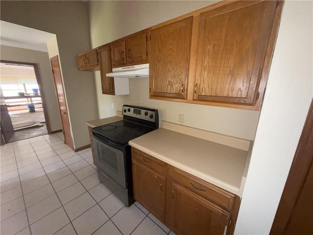 kitchen featuring brown cabinets, under cabinet range hood, light tile patterned flooring, light countertops, and stainless steel electric stove