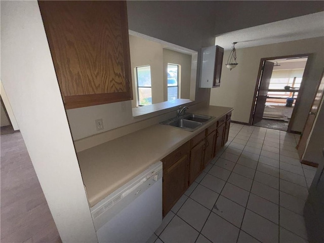 kitchen featuring a sink, light tile patterned floors, light countertops, baseboards, and dishwasher
