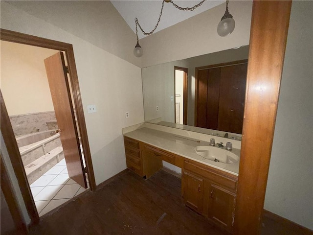 full bath featuring wood finished floors, vanity, baseboards, a garden tub, and lofted ceiling
