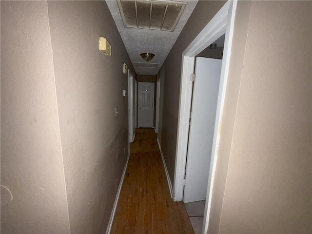 hallway featuring visible vents, wood finished floors, and baseboards