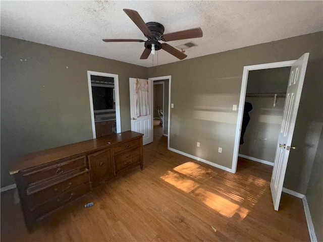 unfurnished bedroom with light wood finished floors, a closet, a walk in closet, baseboards, and a textured ceiling