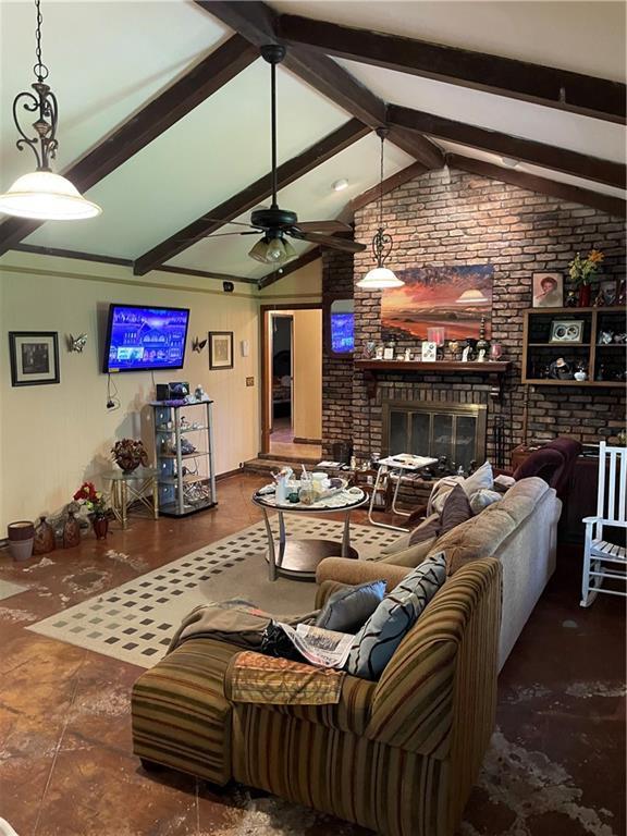 living area featuring a fireplace, brick wall, a ceiling fan, and vaulted ceiling with beams