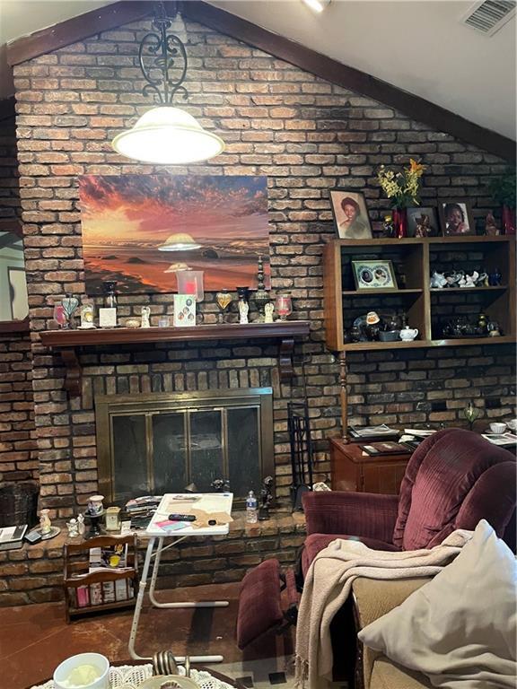living room featuring a fireplace, visible vents, vaulted ceiling, and brick wall