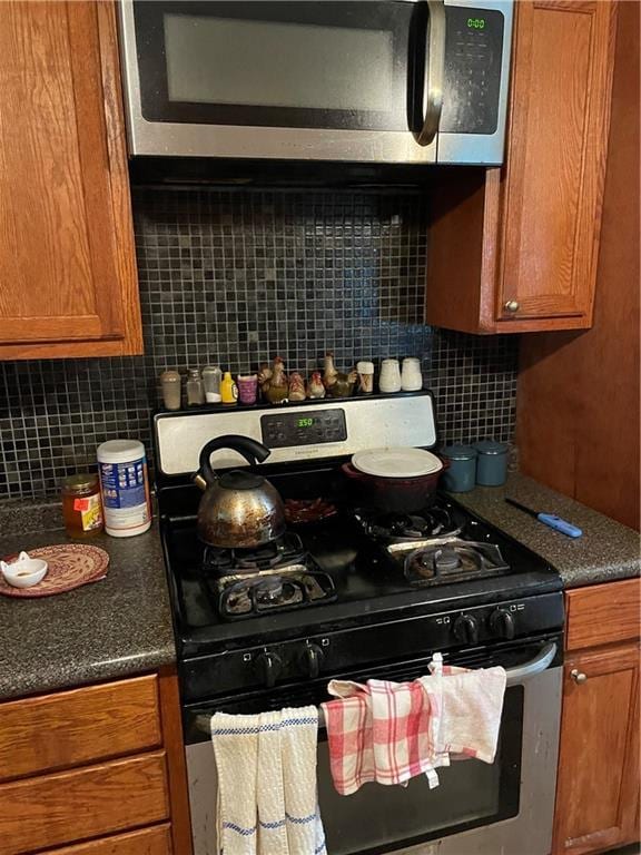kitchen featuring dark countertops, stainless steel appliances, backsplash, and brown cabinets
