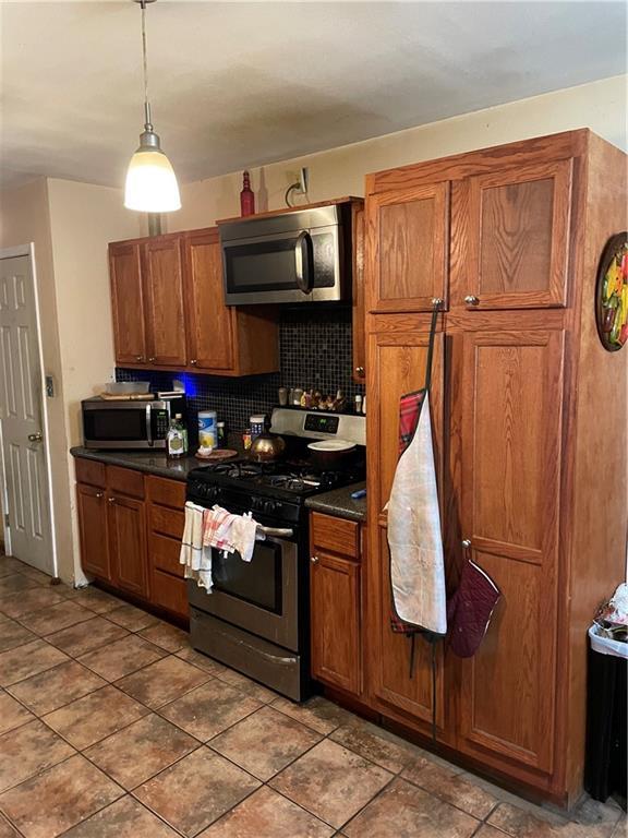 kitchen with tasteful backsplash, dark countertops, appliances with stainless steel finishes, and brown cabinetry