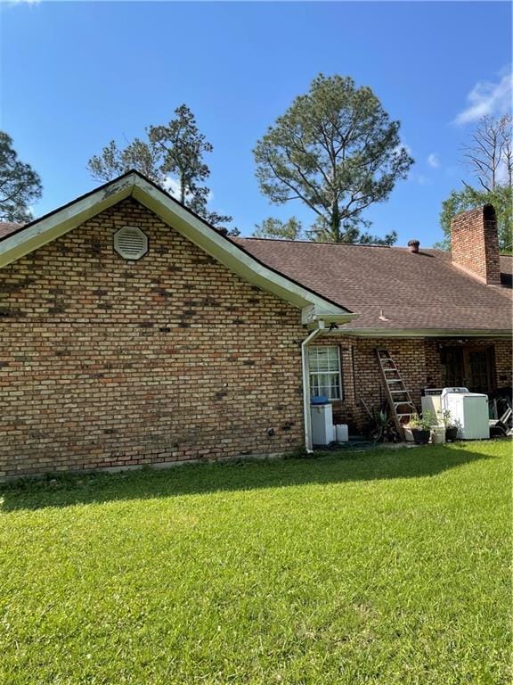 exterior space featuring a chimney, brick siding, a shingled roof, and a yard
