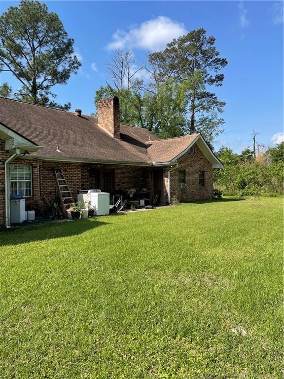 rear view of property featuring brick siding, roof with shingles, a yard, and a chimney