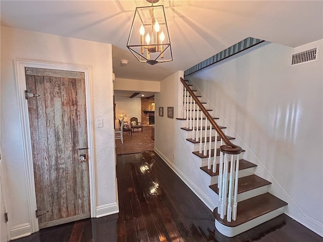staircase with baseboards, visible vents, an inviting chandelier, and wood-type flooring