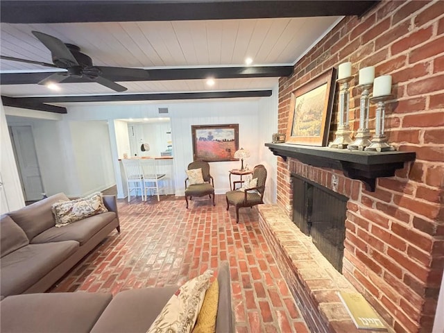 living room featuring brick wall, beamed ceiling, brick floor, a fireplace, and a ceiling fan