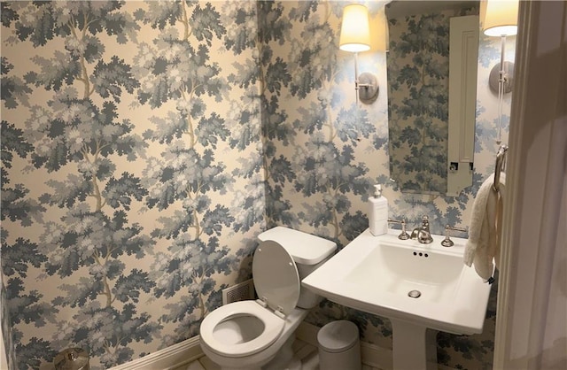 half bath featuring baseboards, wallpapered walls, toilet, and a sink