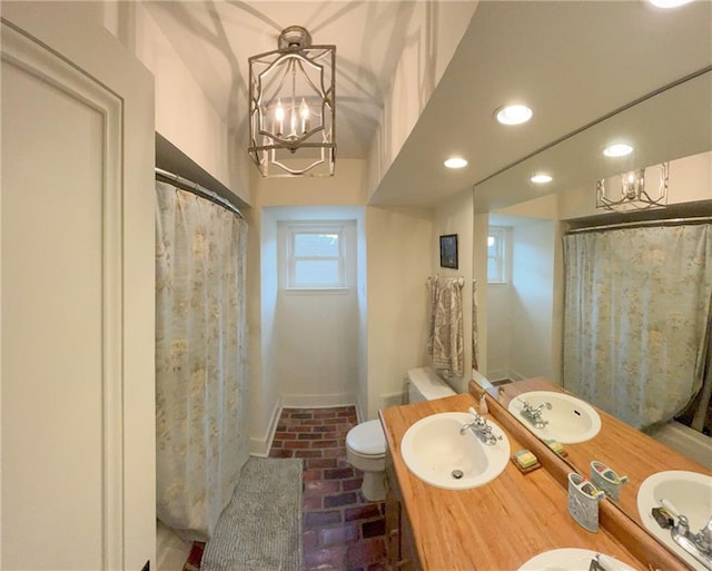 full bathroom with a notable chandelier, toilet, brick floor, and a sink