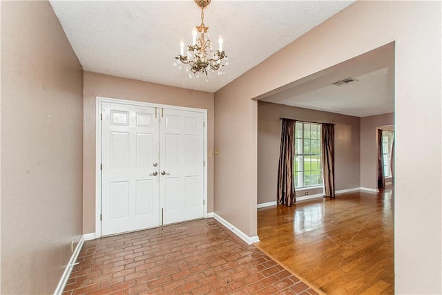 foyer featuring a notable chandelier, visible vents, brick floor, and baseboards