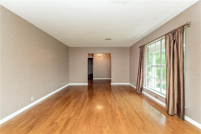 spare room with visible vents, a chandelier, wood finished floors, and baseboards