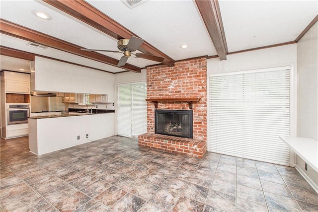 unfurnished living room with ceiling fan, a brick fireplace, a sink, beam ceiling, and visible vents