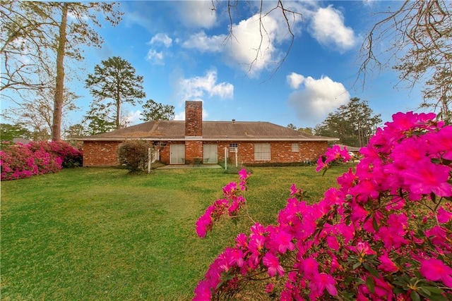 rear view of house featuring a chimney, brick siding, and a lawn