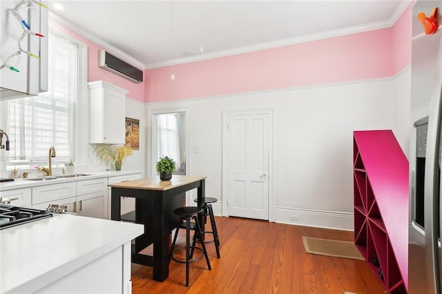 kitchen featuring white cabinets, a sink, light countertops, ornamental molding, and an AC wall unit